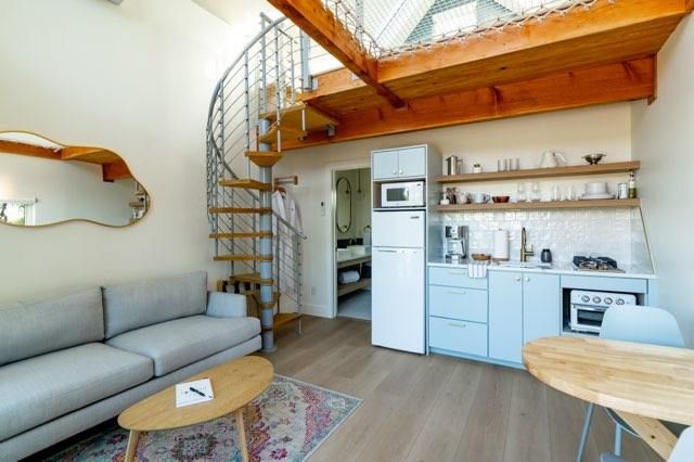 Modern loft apartment interior with spiral staircase, exposed wooden beams, and open concept living space.