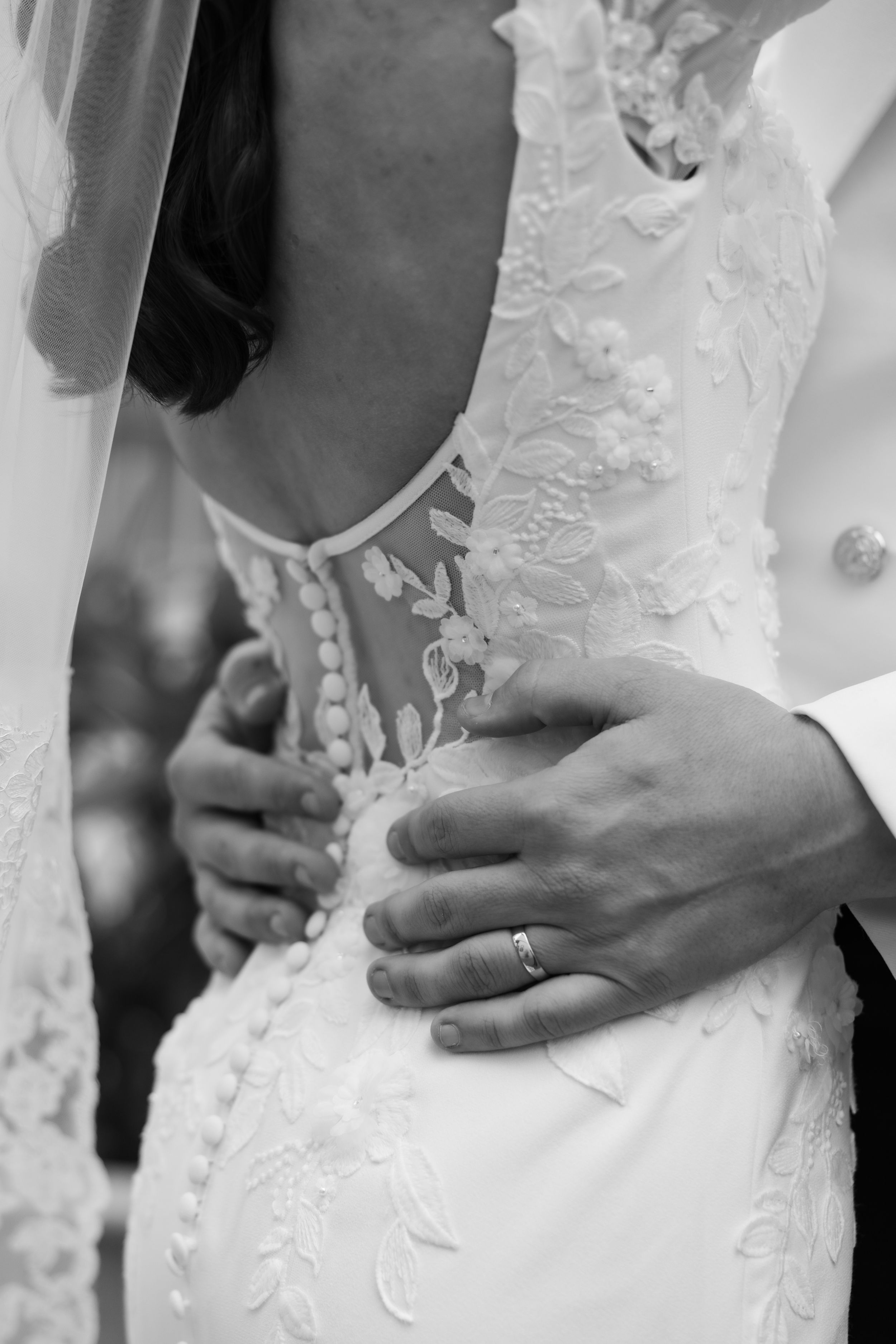 A close-up view of a bride's torso in a white lace wedding dress with delicate floral embellishments.