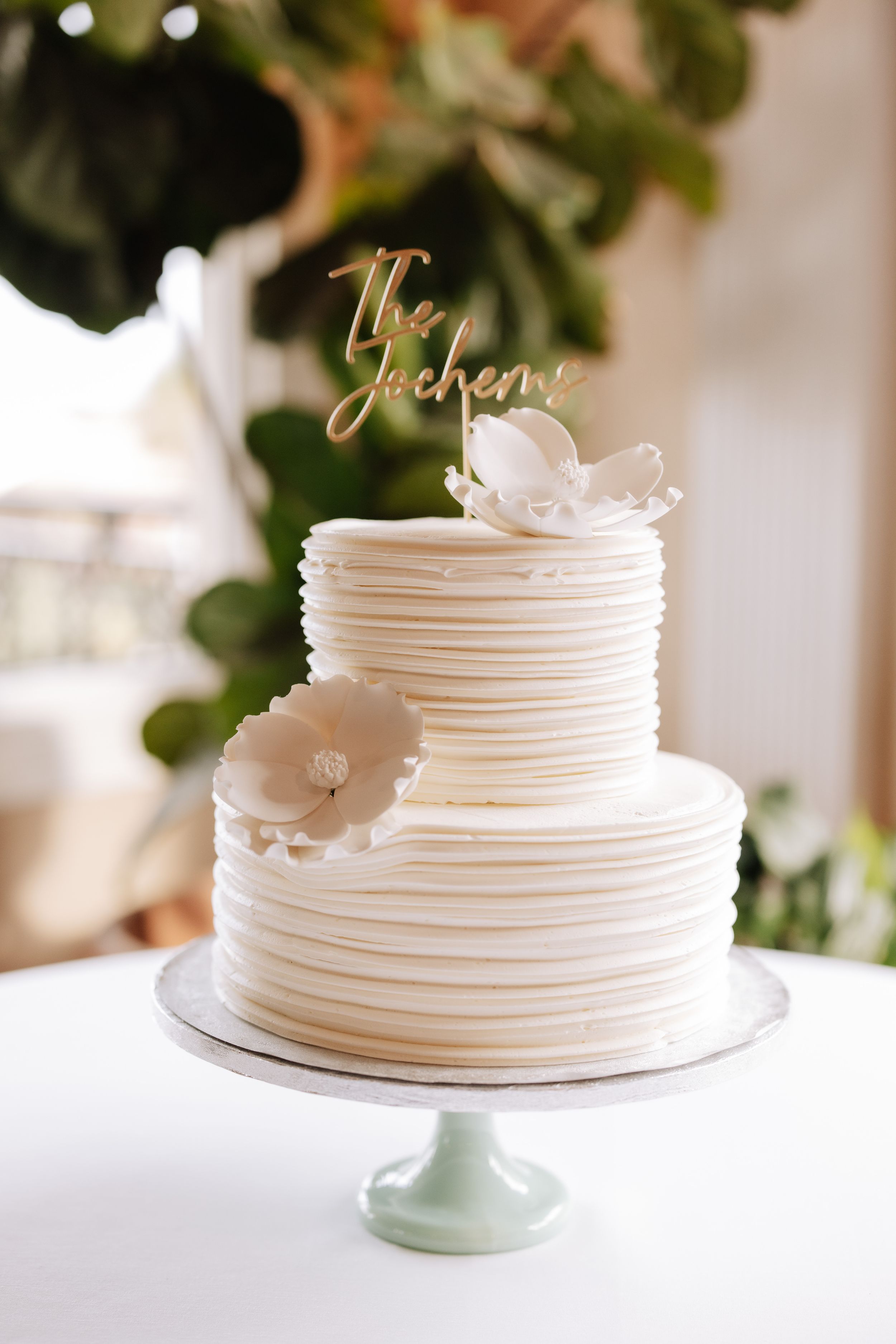 Elegant white wedding cake with delicate horizontal lines and floral accents displayed on a light blue cake stand.