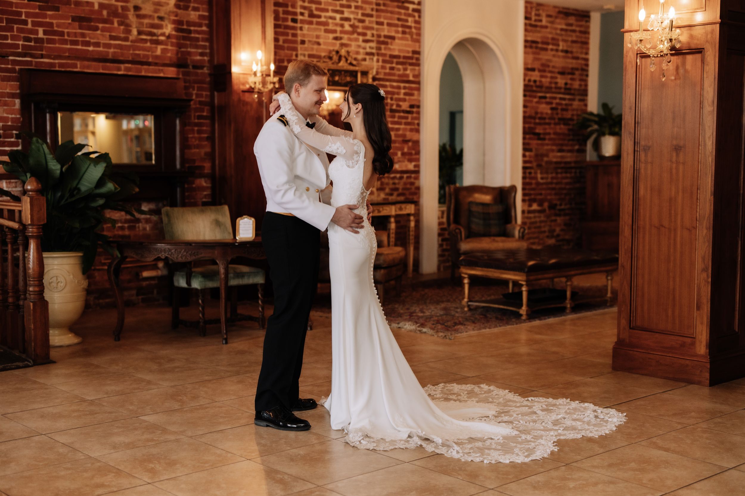 A romantic couple shares a tender moment on their wedding day in a rustic brick-walled venue with elegant lighting.