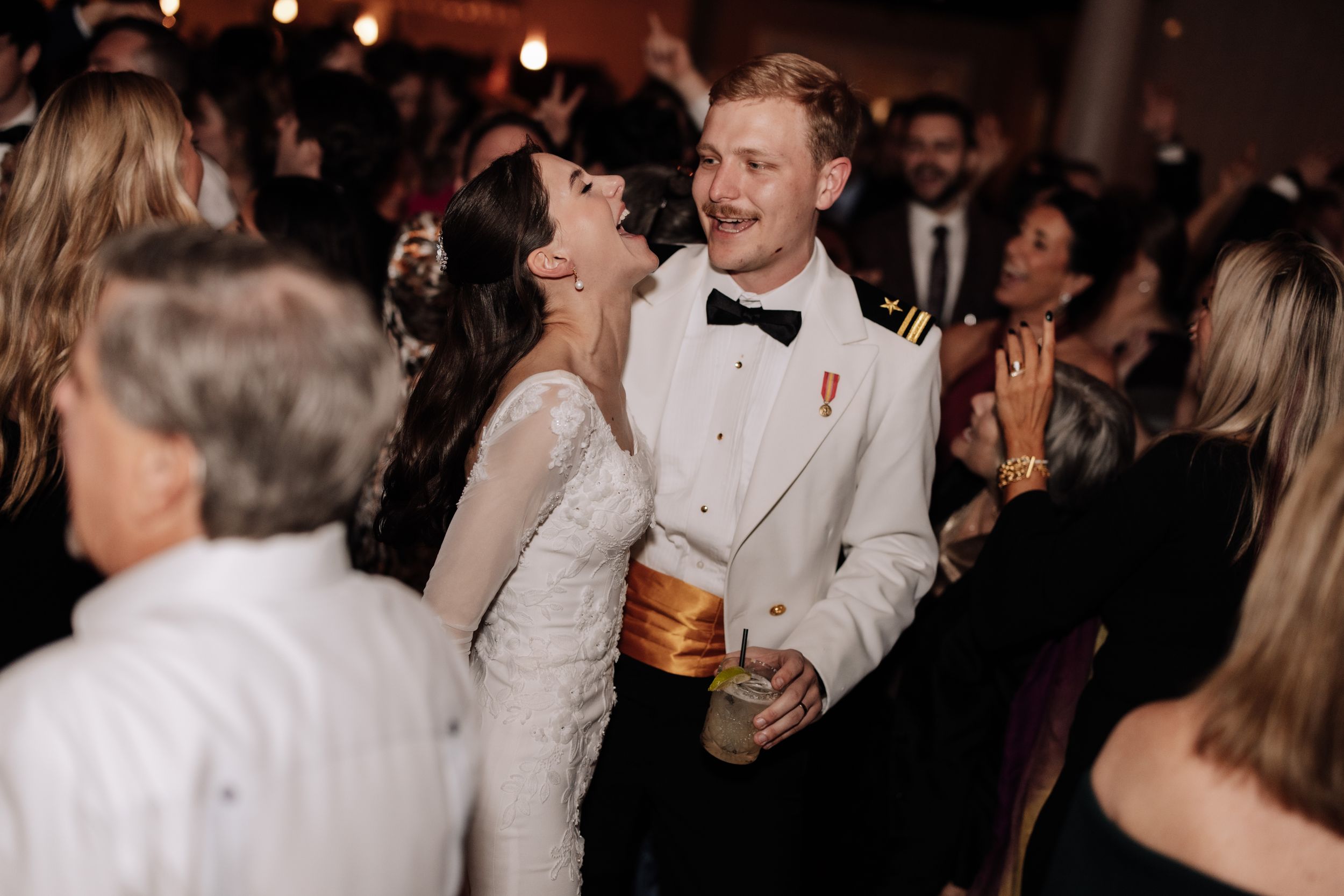 A crowded reception party with guests in formal attire mingling and celebrating in an elegant indoor venue.