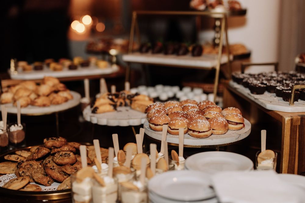 A dessert table displays an elegant assortment of cookies, pastries and sweet treats with glowing candles at an event.
