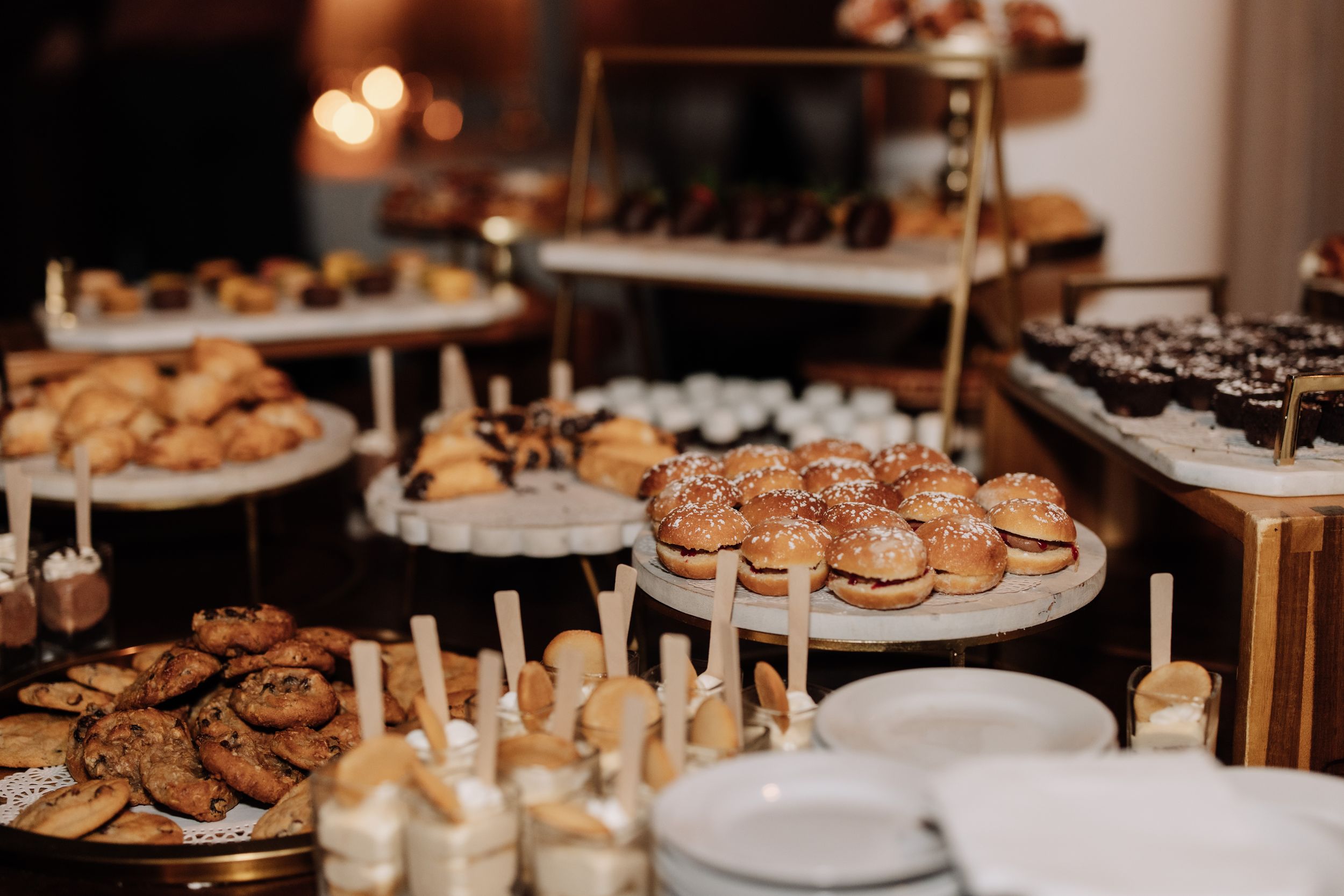 A dessert table displays an elegant assortment of cookies, pastries and sweet treats with glowing candles at an event.