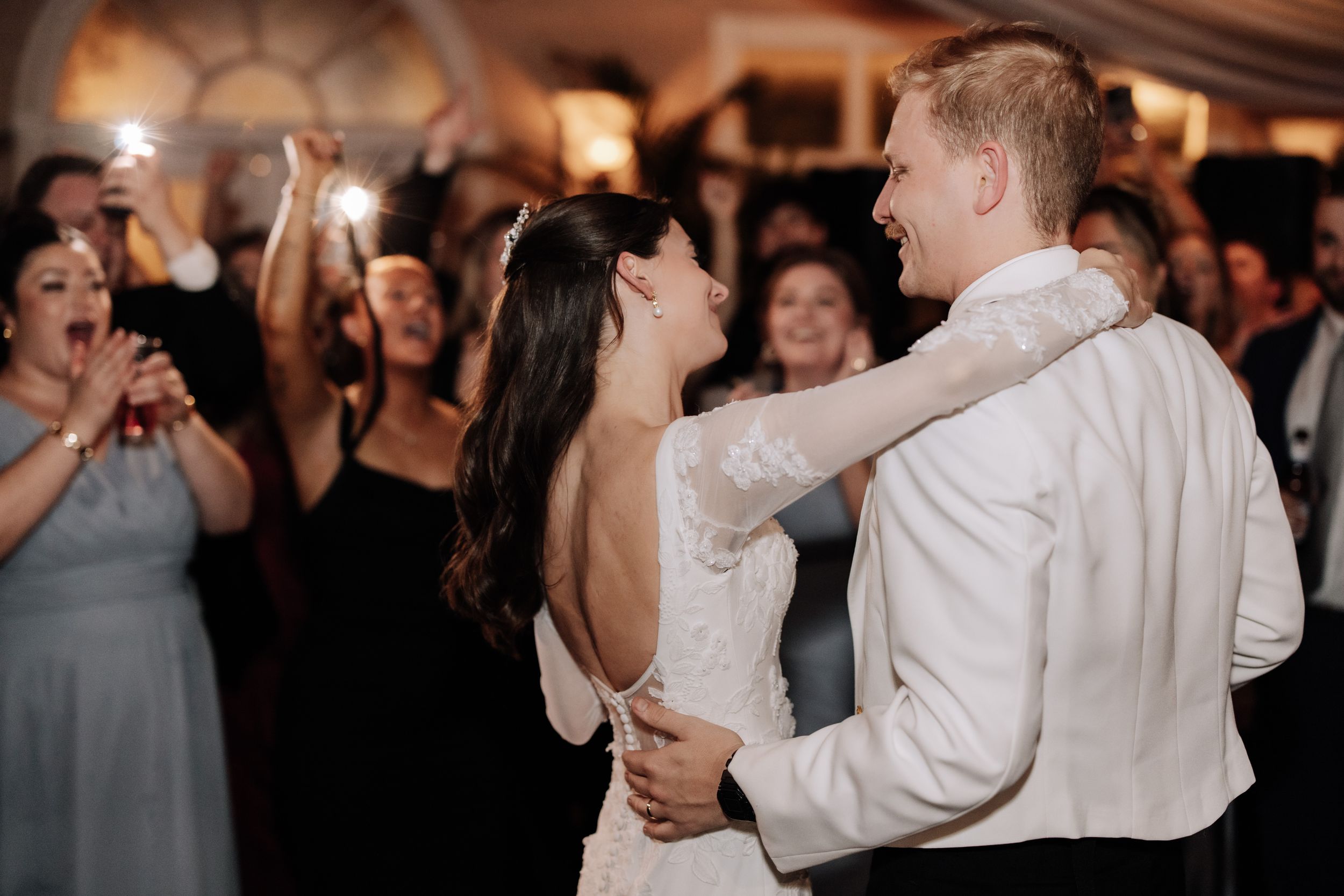 Wedding guests dance and celebrate together on a dimly lit dance floor during an evening reception.