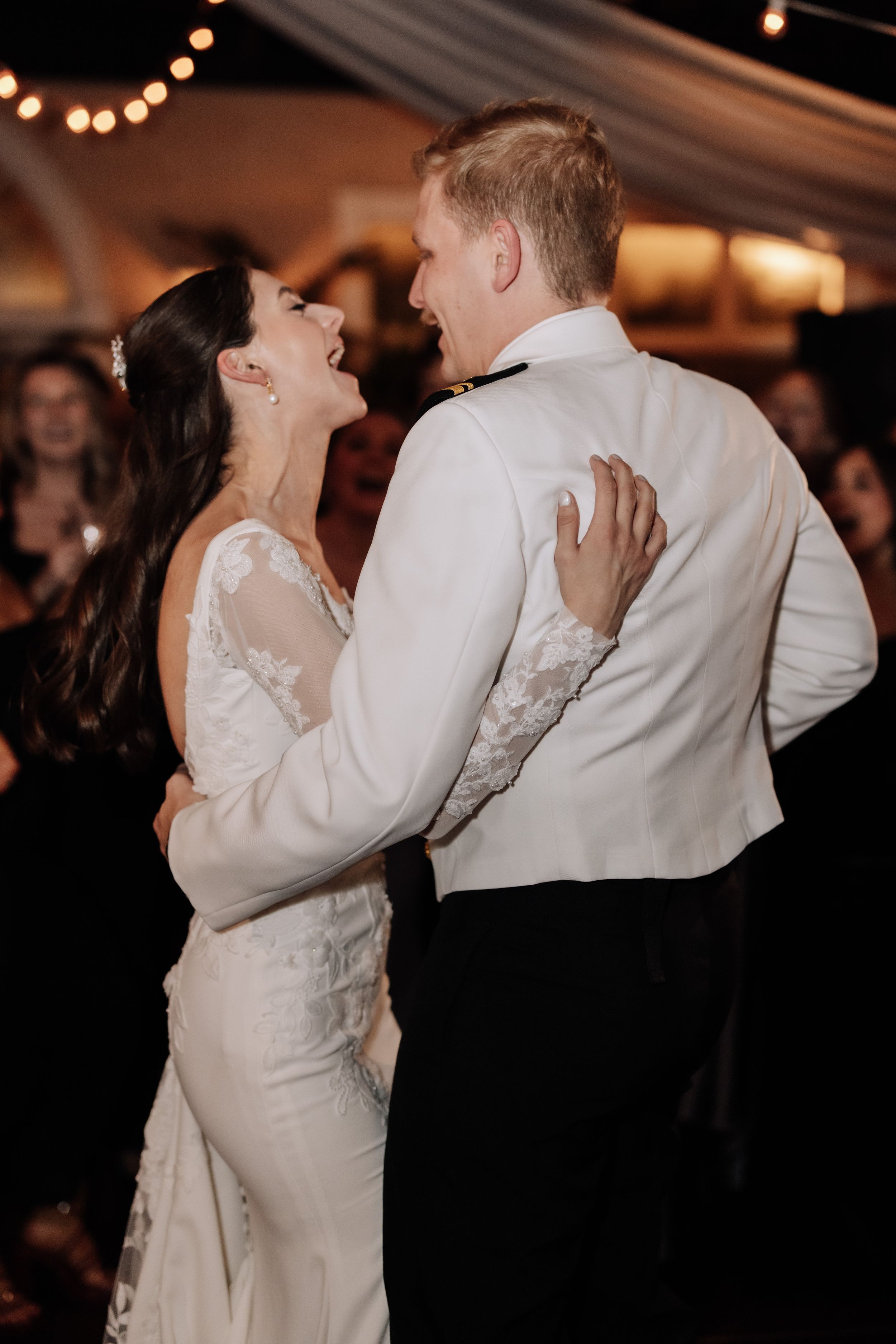 A couple shares an intimate dance moment at their wedding reception under warm string lights.