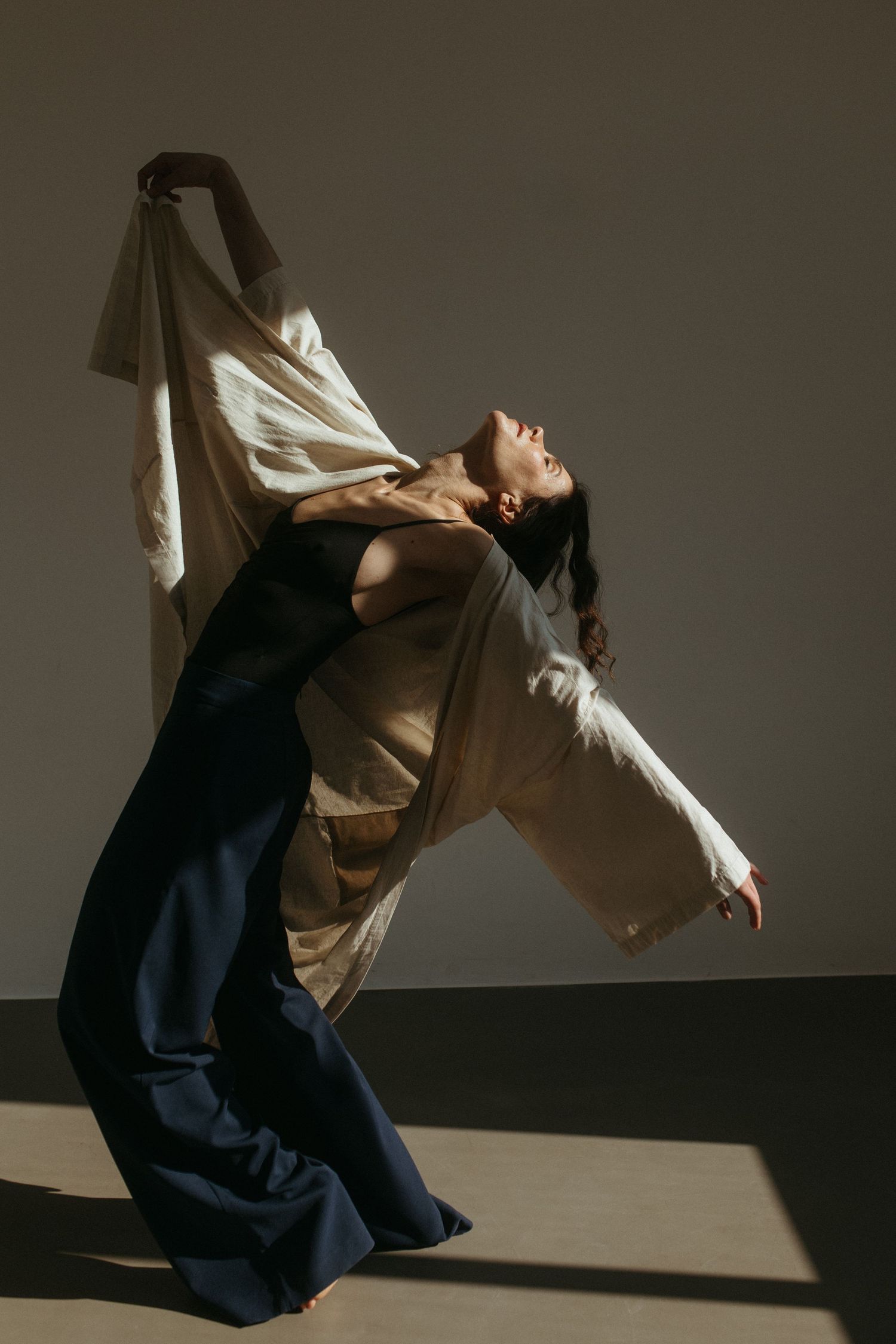 Contemporary dancer in flowing navy dress performs dramatic backbend movement in dramatic studio lighting.