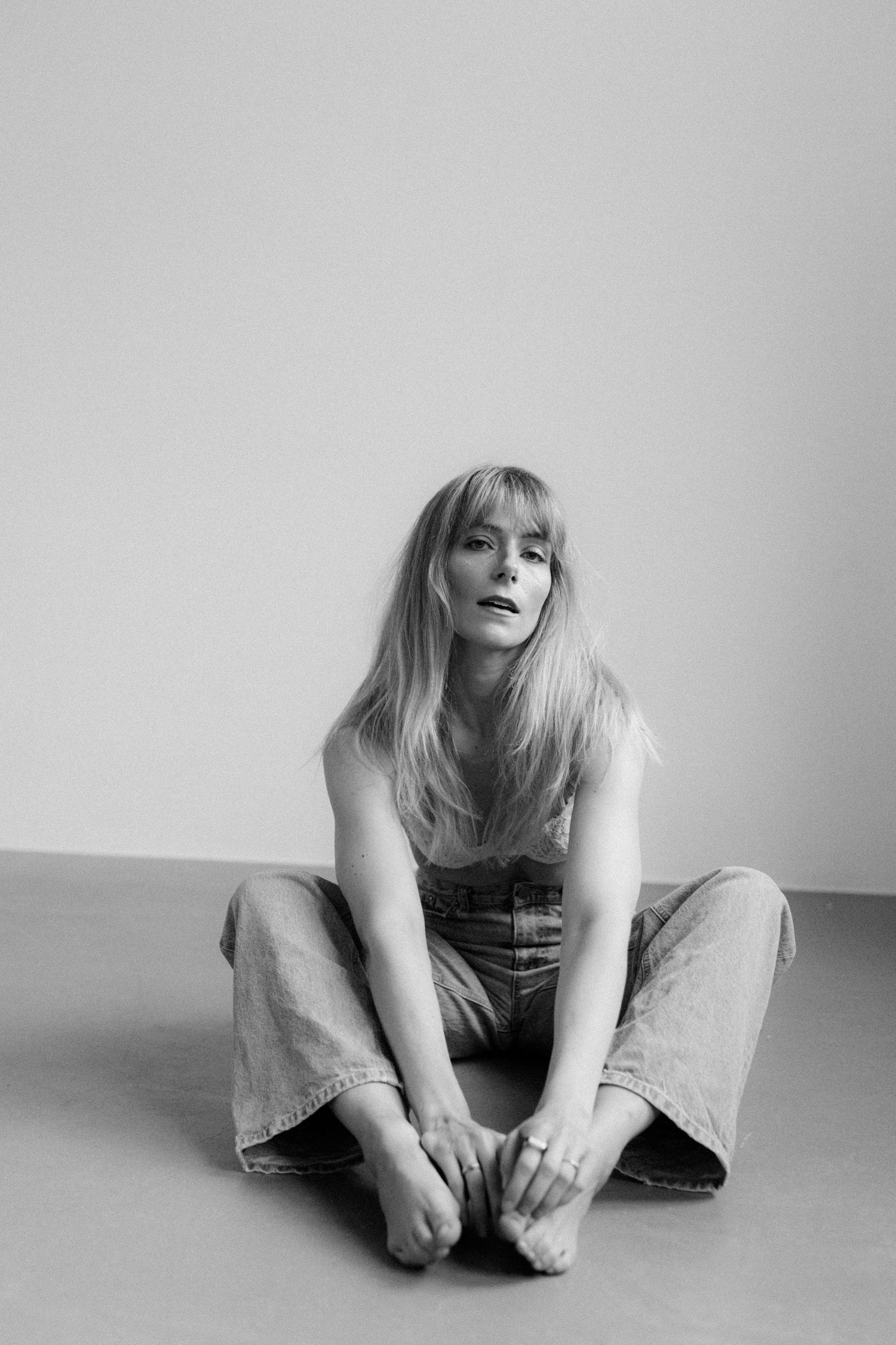 Black and white portrait of someone sitting on floor in casual denim, touching their feet in contemplative pose.