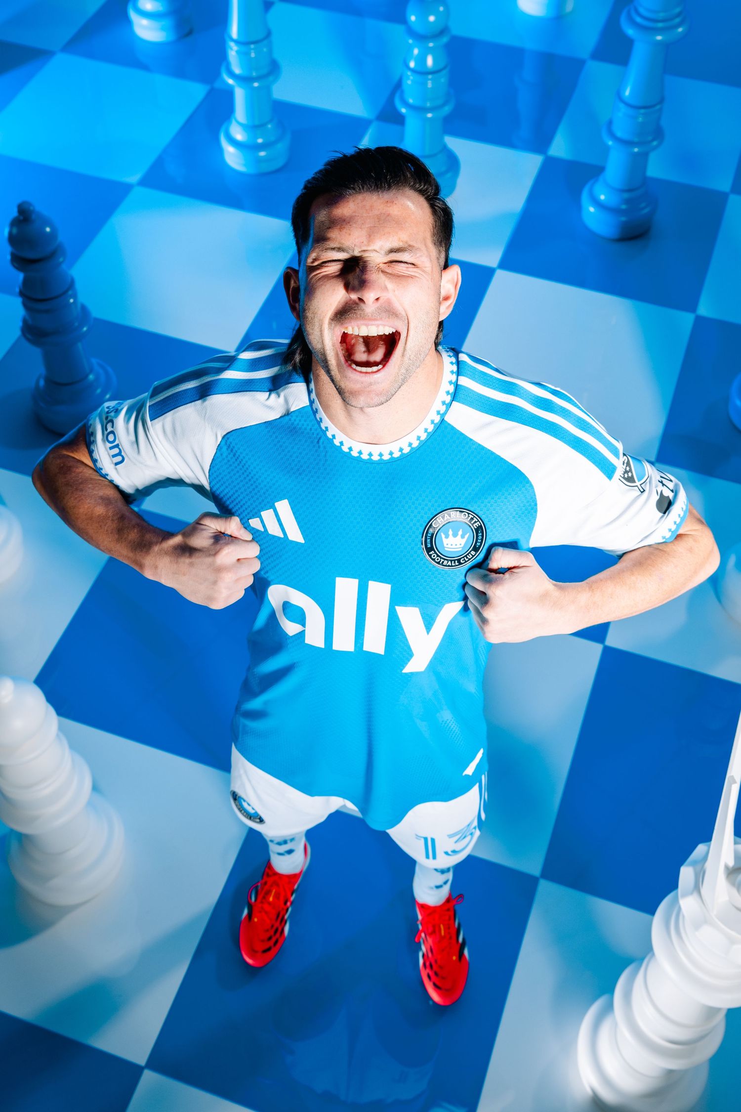 Charlotte FC player in blue Adidas ally jersey celebrating on giant chess board set.