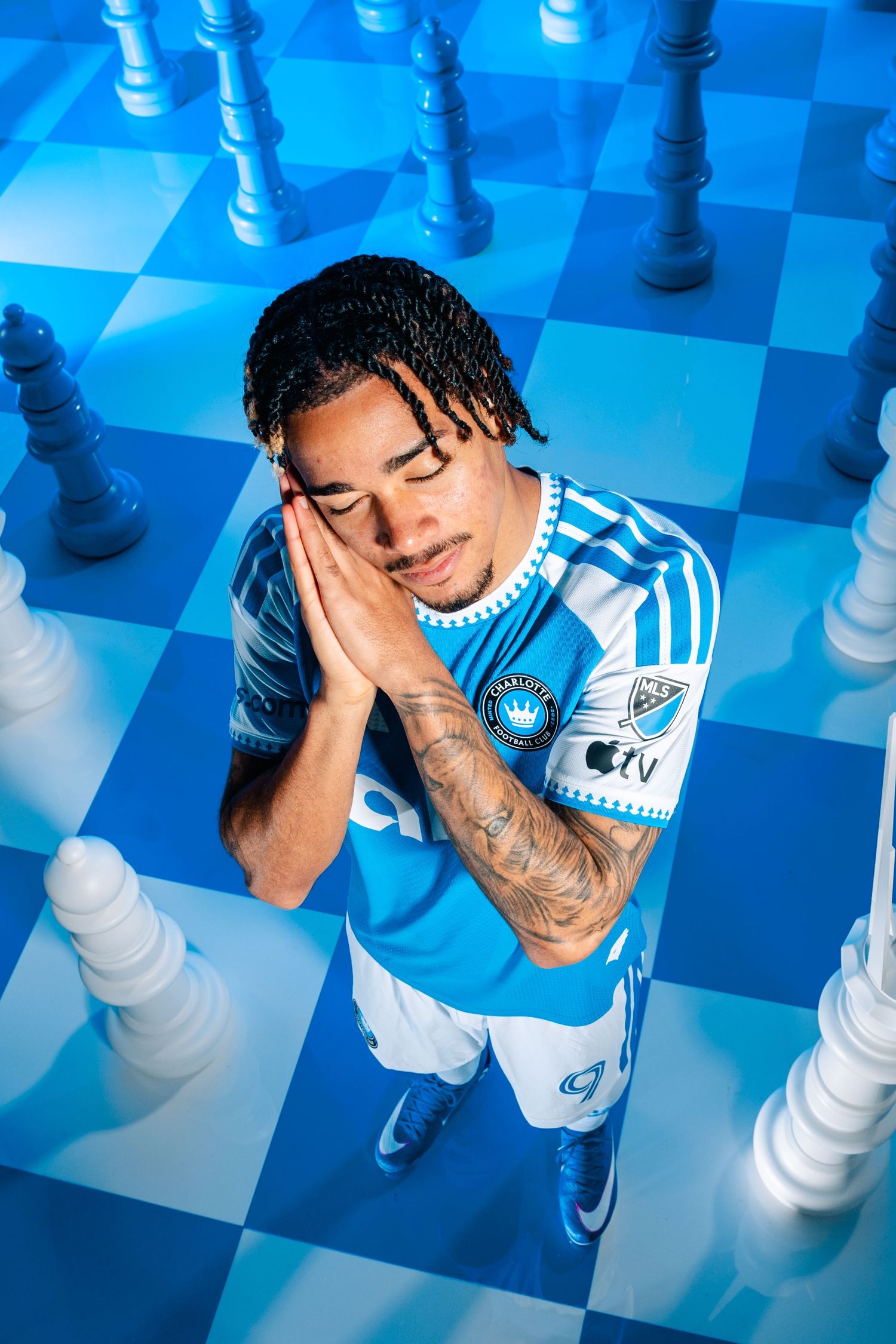 Charlotte FC player posing on giant blue chess board surrounded by oversized white chess pieces.