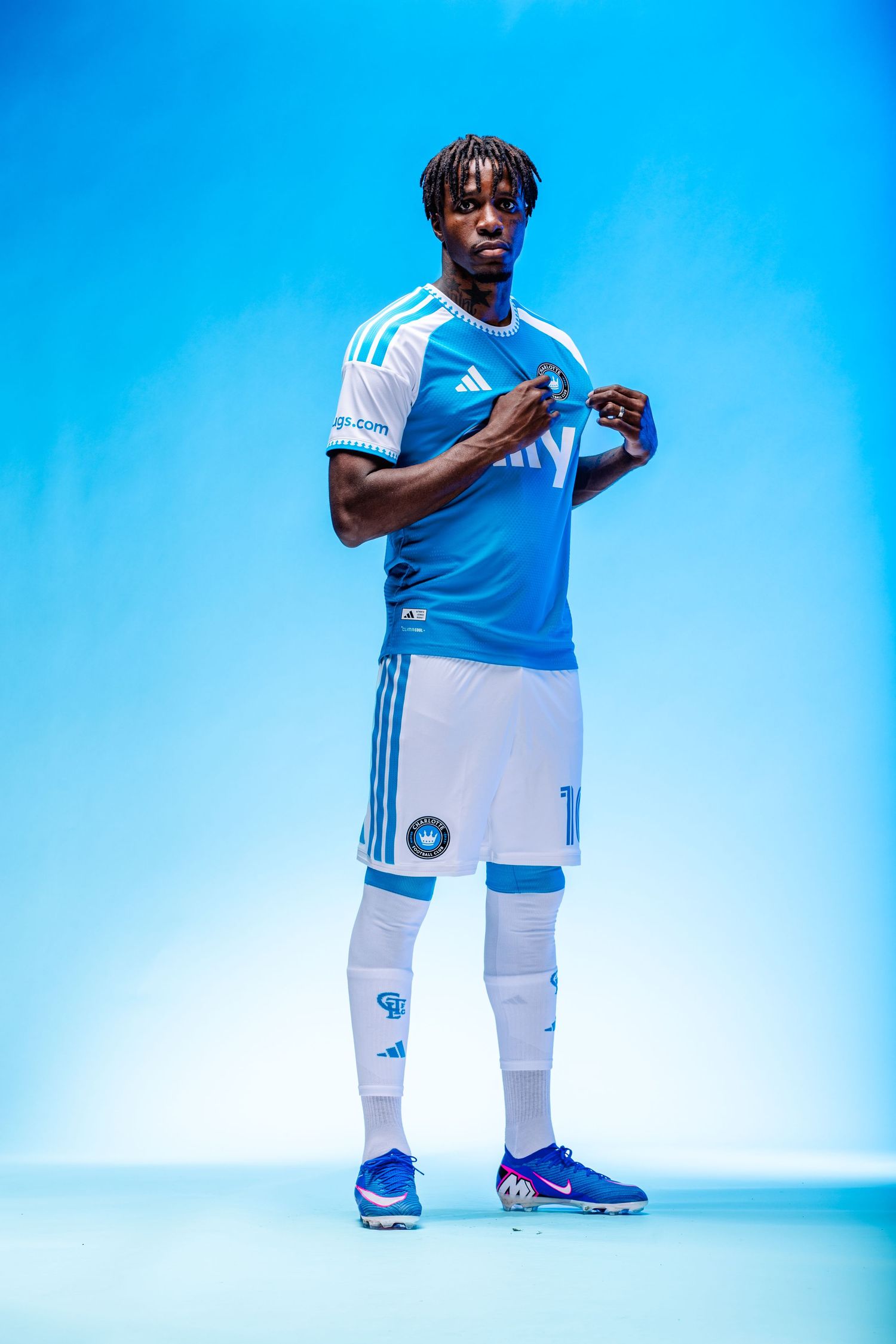 Charlotte FC player proudly wears blue and white Adidas ally jersey while pointing to club crest.