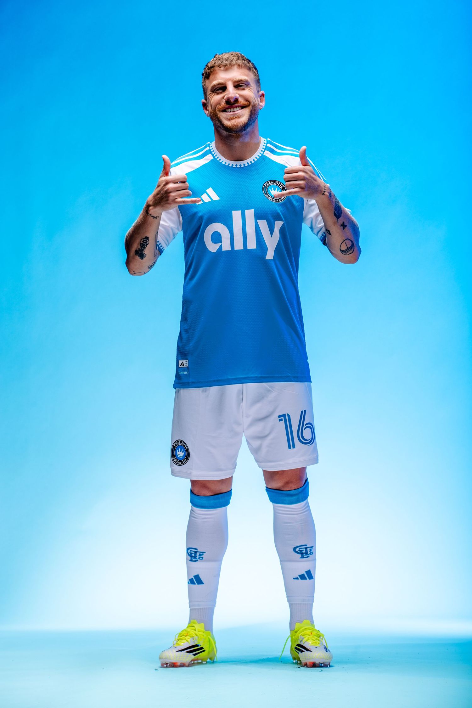 Tattooed Charlotte FC player #16 gives thumbs up in blue ally Adidas kit with yellow cleats.