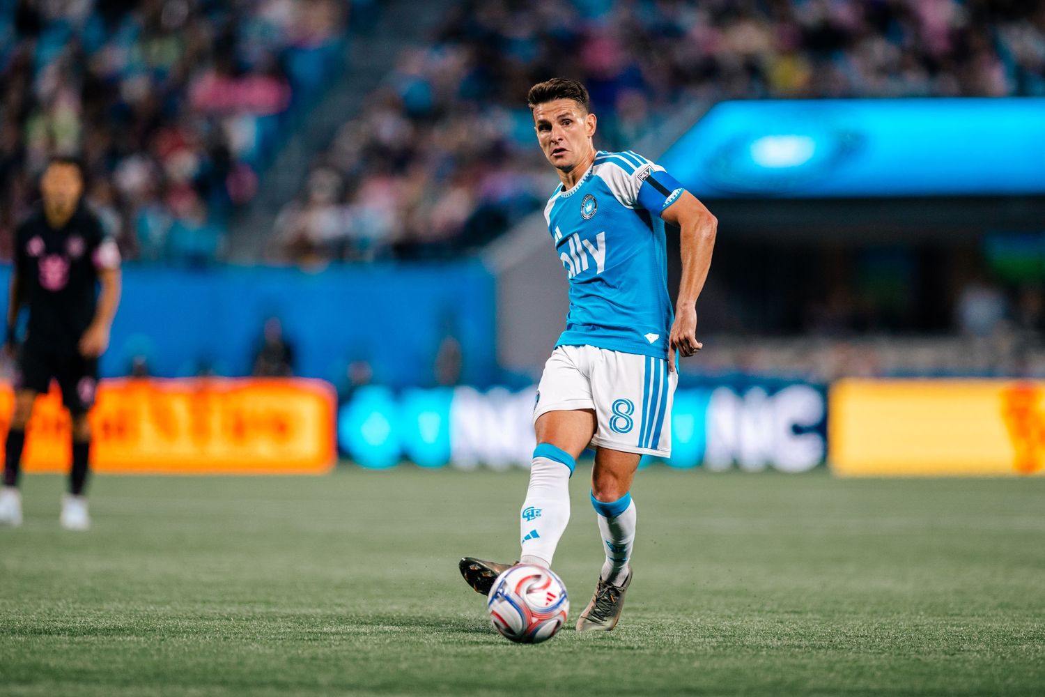 Charlotte FC player #8 dribbles soccer ball in blue ally kit during MLS match.