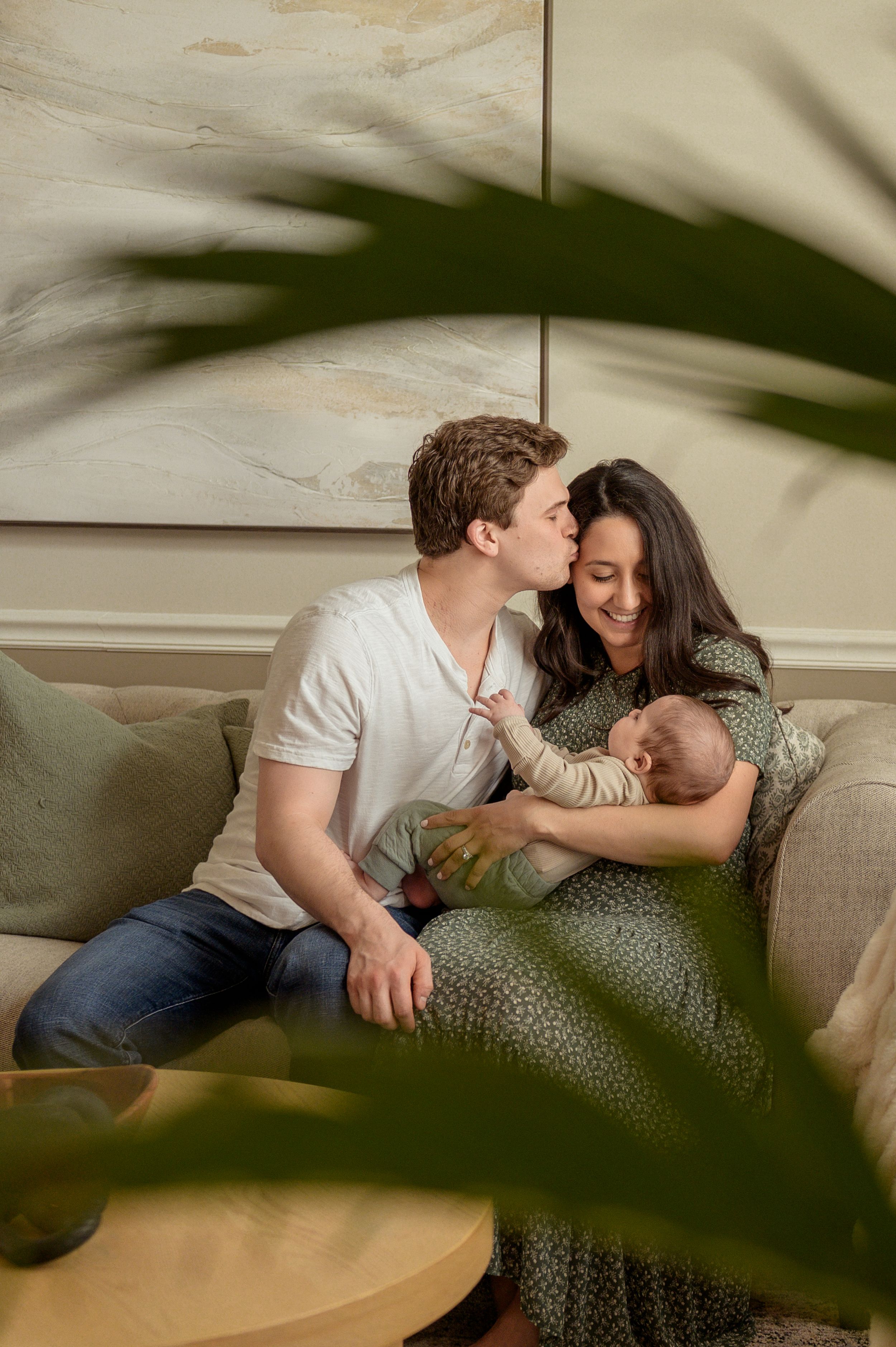 A couple with a newborn baby cuddling on a couch in a cozy living room.