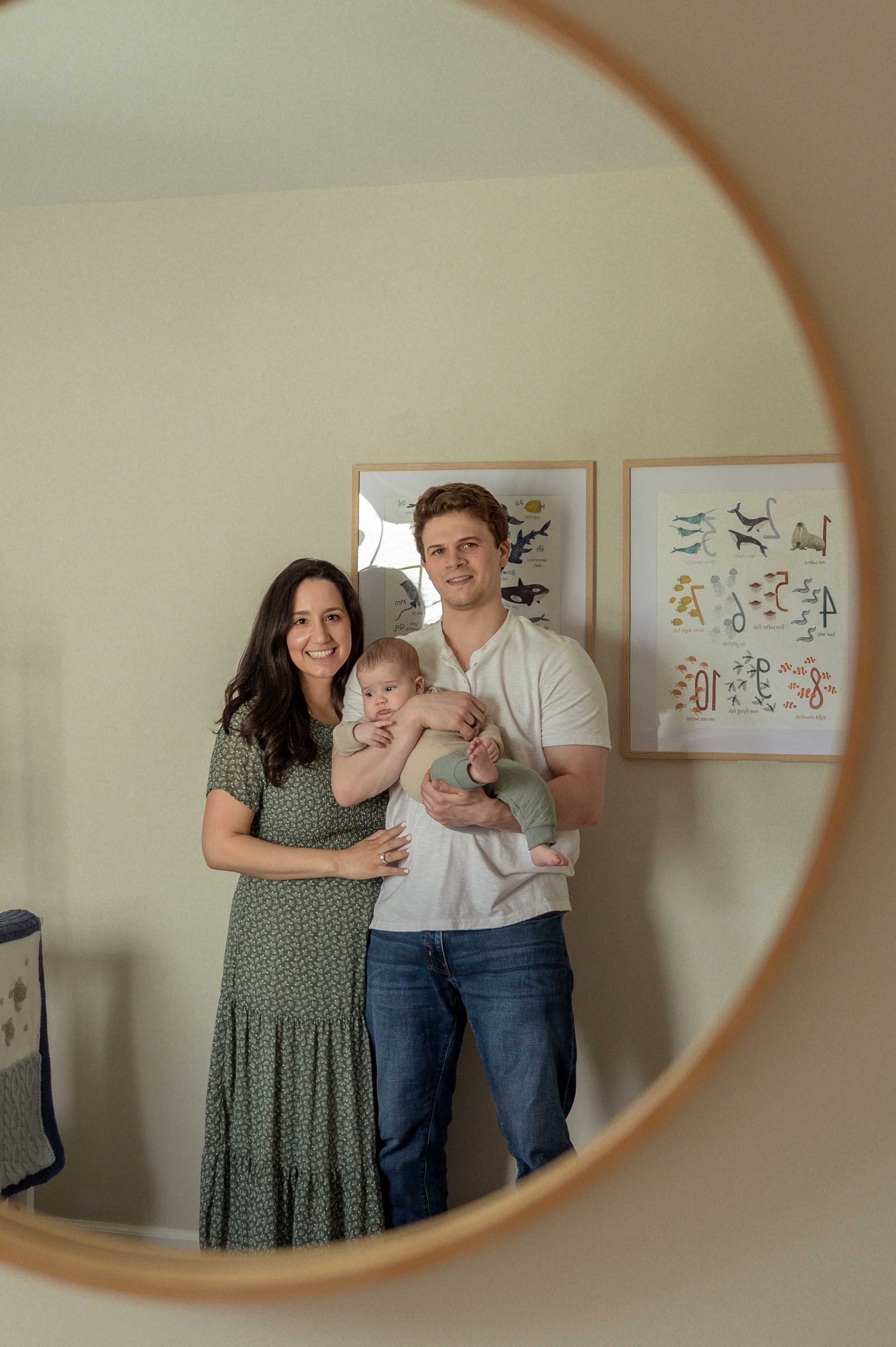 A family portrait of a couple holding a young child, reflected in a round mirror on the wall.