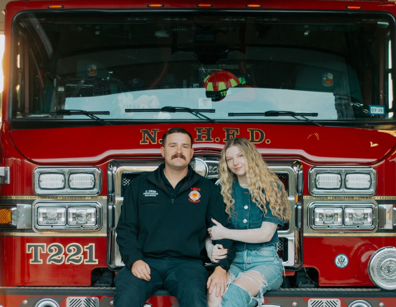 A firefighter and companion pose in front of a bright red NYPD fire truck T221.