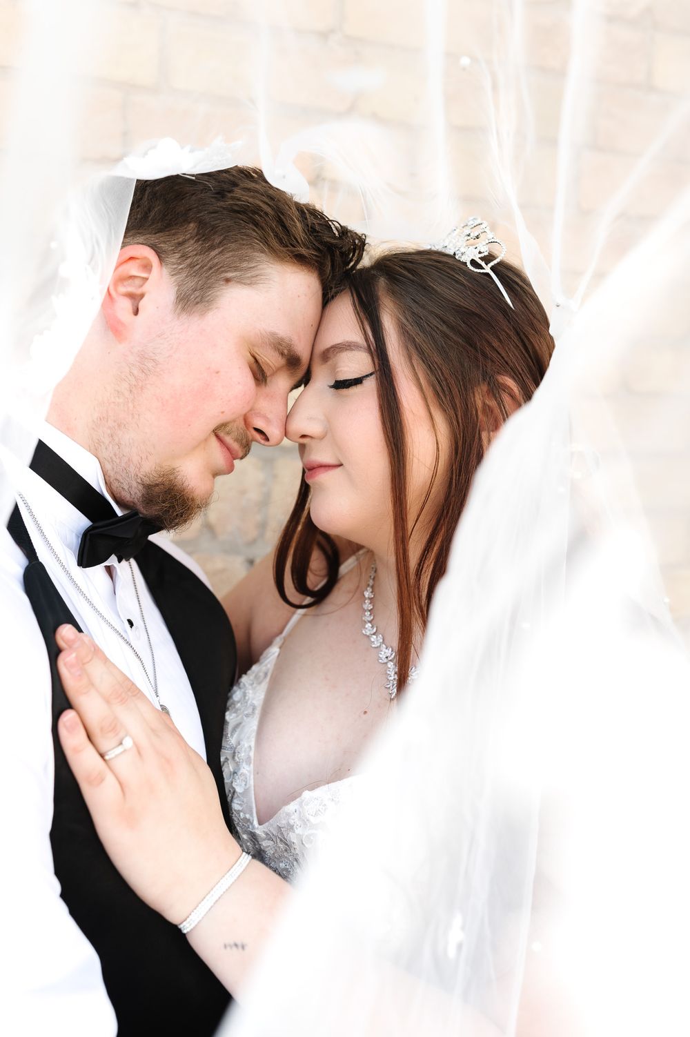 A romantic wedding portrait showing a tender moment between newlyweds in formal attire with veil and tiara details.