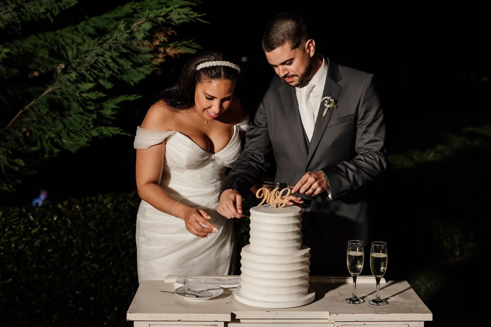 A couple cuts their elegant white wedding cake together in a romantic outdoor garden setting.