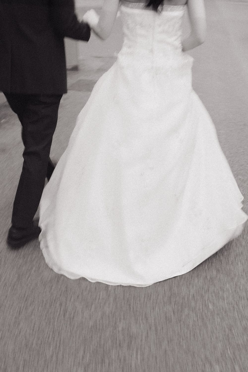 Black and white photo showing the bottom half of a flowing white wedding dress and dark suit during a dance. Couple photoshoot barceLONa