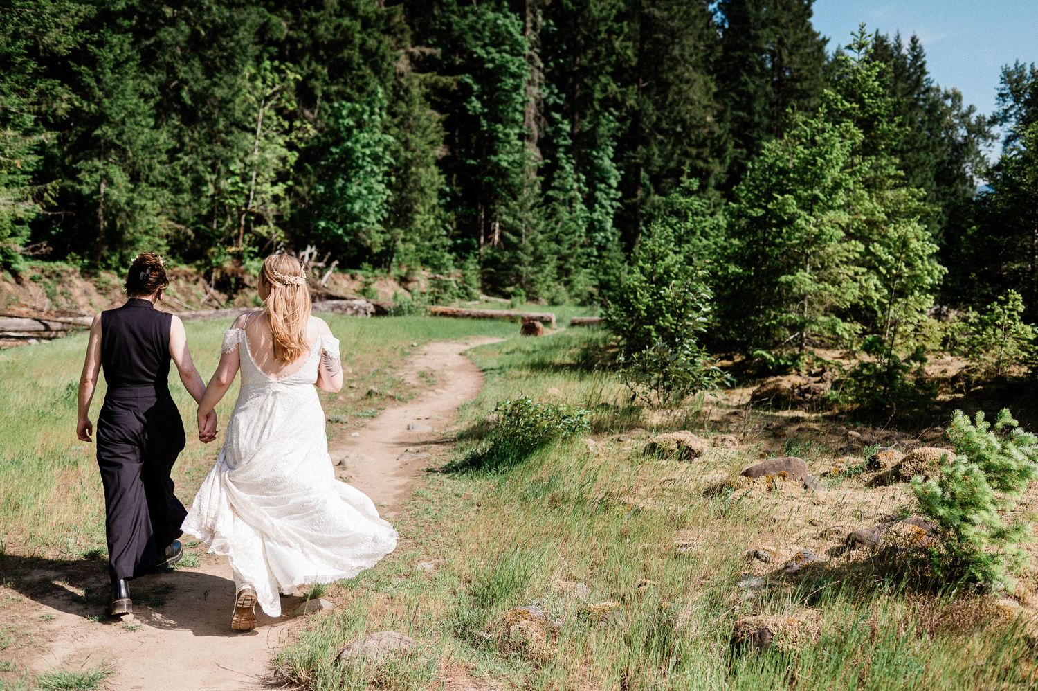 A couple walks together on a scenic mountain trail surrounded by evergreen trees and natural landscape.