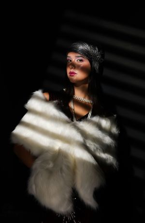 Girl in blind like shadows, wearing a white shall, pearl necklace and a red flapper outfit, looking straight at camera