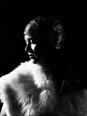 Side profile black and white photo of a girl wearing a white shall, silver turban, and a pearl necklace, looking down with eyes closed