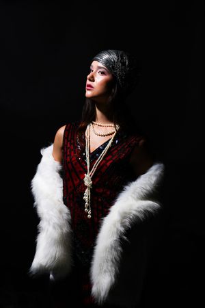 Girl in like shadows, wearing a white shall, pearl necklace and a red flapper outfit, looking left and up