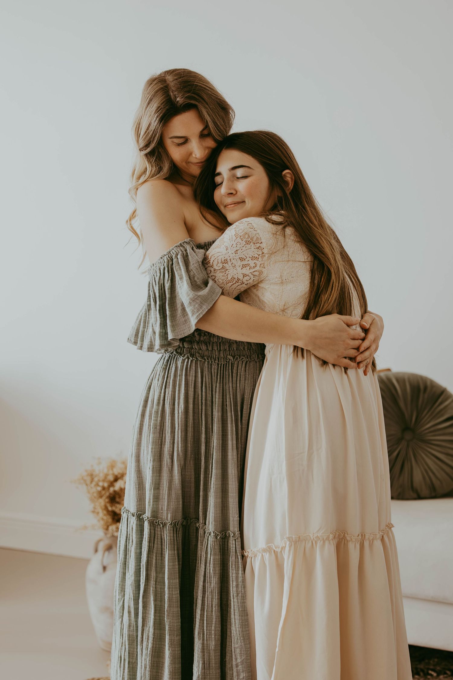 A group embraces in a tender moment wearing flowing dresses in neutral tones and floral patterns.