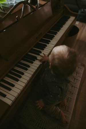 Toddler in green outfit reaching up to play keys on a vintage upright wooden piano.