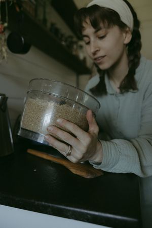 Young woman in apron holding food processor bowl filled with ground grains in a cozy kitchen.