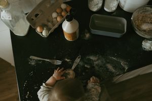 A baby plays with flour and baking ingredients spread across a dark kitchen counter.