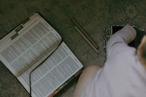 Open Bible with pencils beside a person holding a small journal on a textured surface.