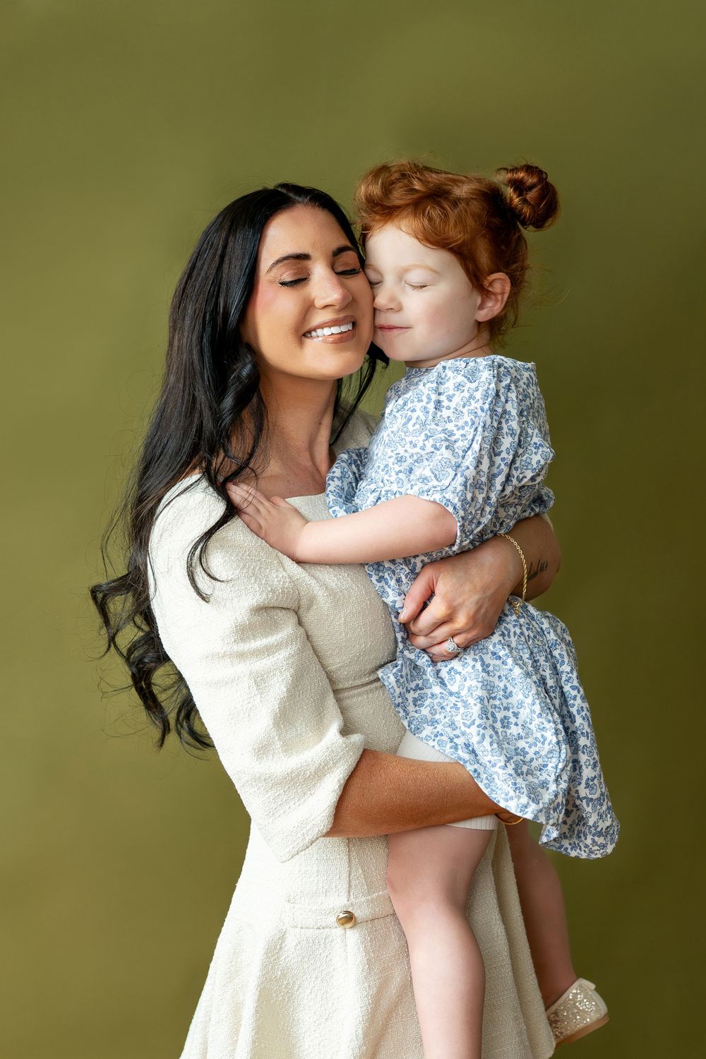 Mother and redhead toddler girl sharing tender cheek kiss embrace.
