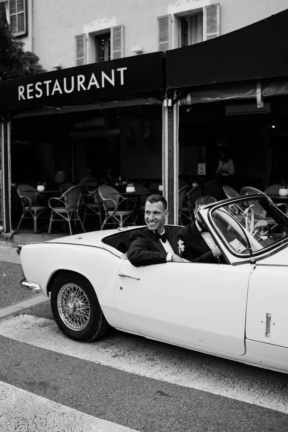 A classic white convertible sports car parked outside a restaurant in a black and white photograph.