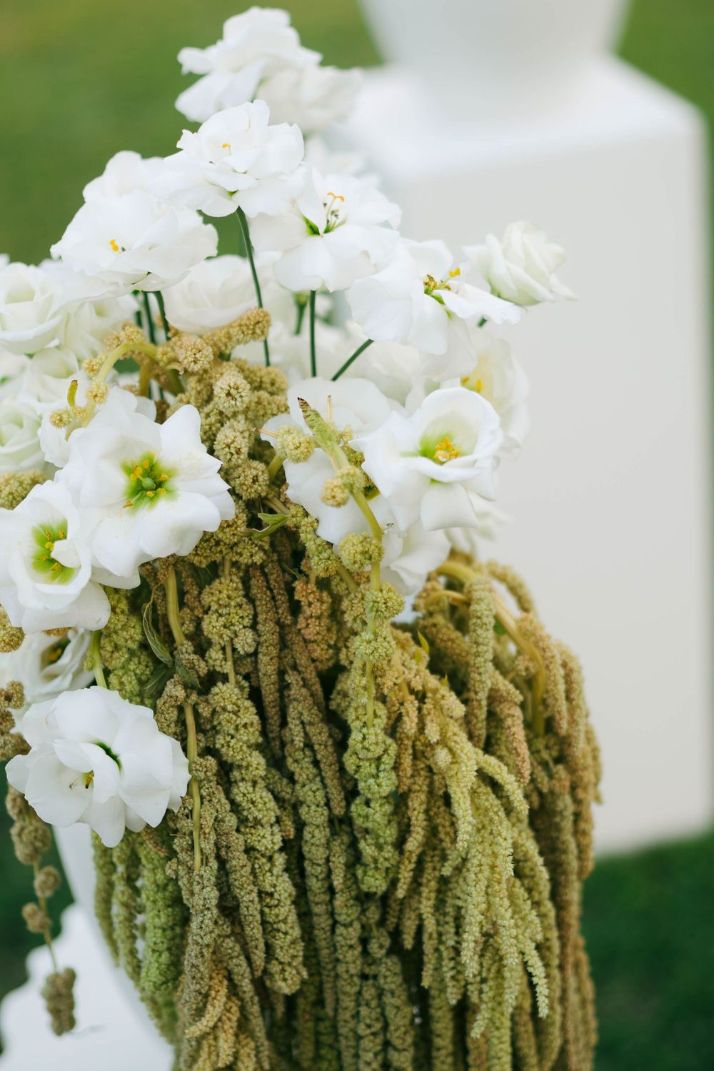 White lisianthus flowers arranged with cascading green amaranthus in an elegant floral arrangement.