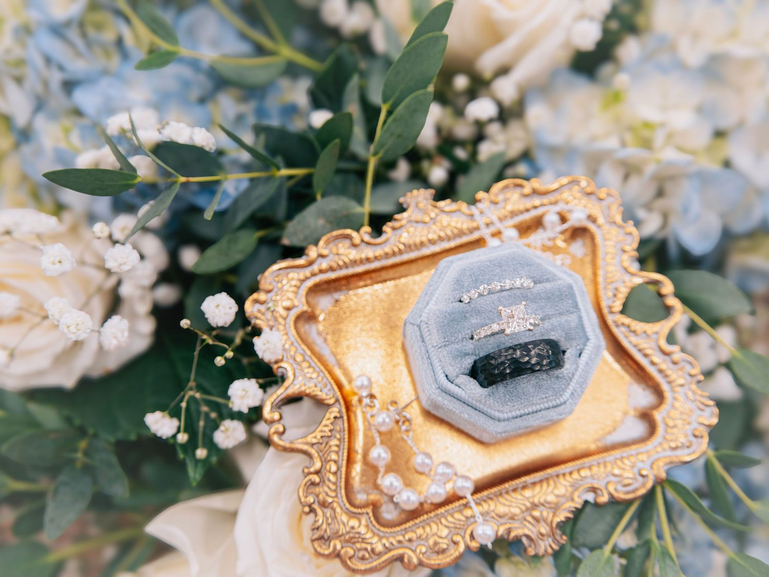 Wedding rings displayed in an ornate gold frame surrounded by delicate flowers and greenery.