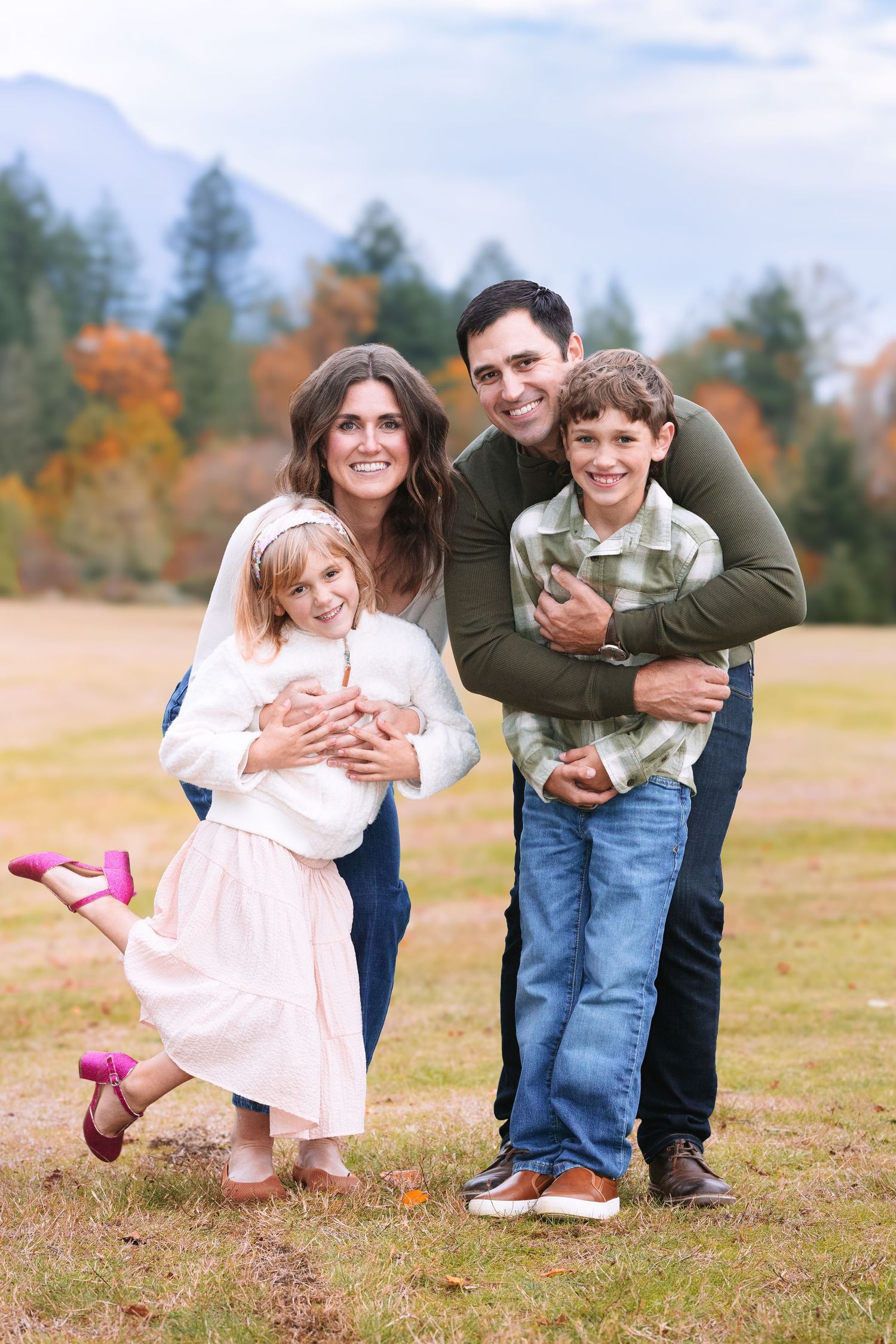 A family plays together in a grassy field during autumn with fall foliage visible in the background.