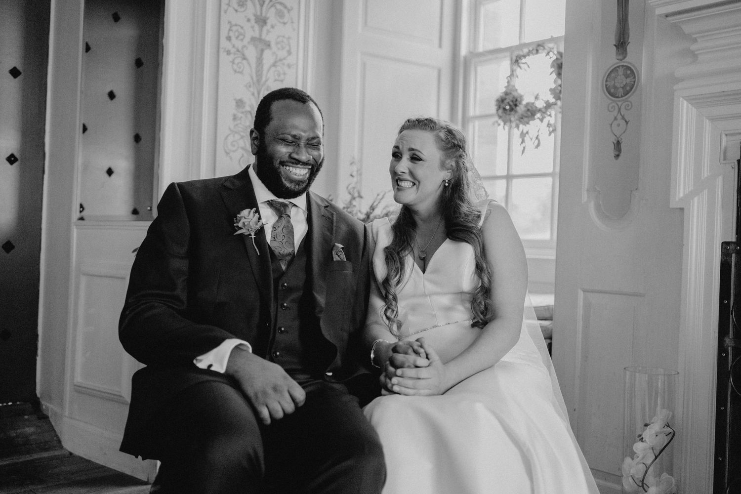 Black and white photo of newlyweds sitting together in elegant indoor setting.