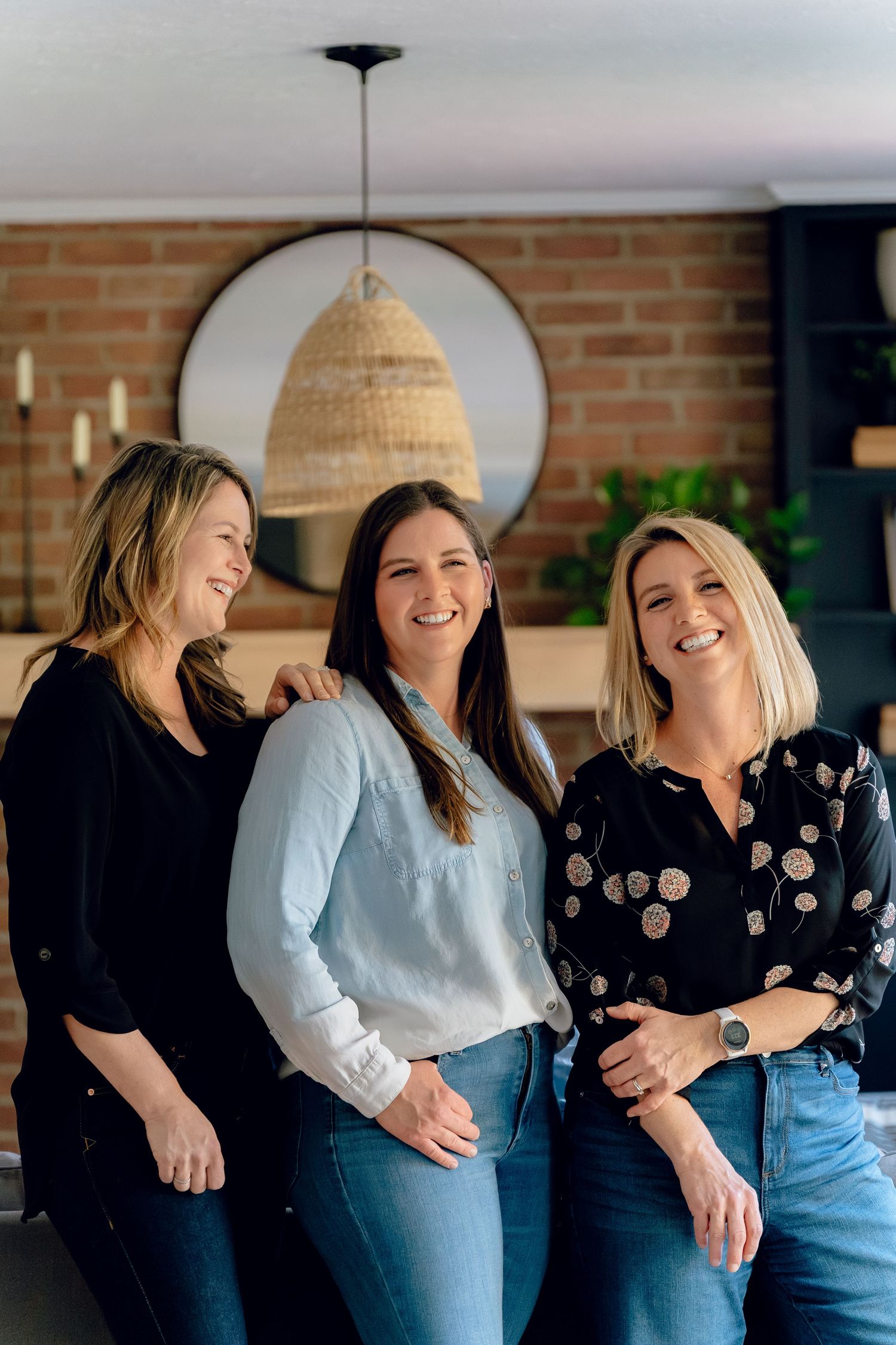 Sister Home Systems ladies' in casual attire laughing and embracing at an in-home brand session against a brick wall backdrop.