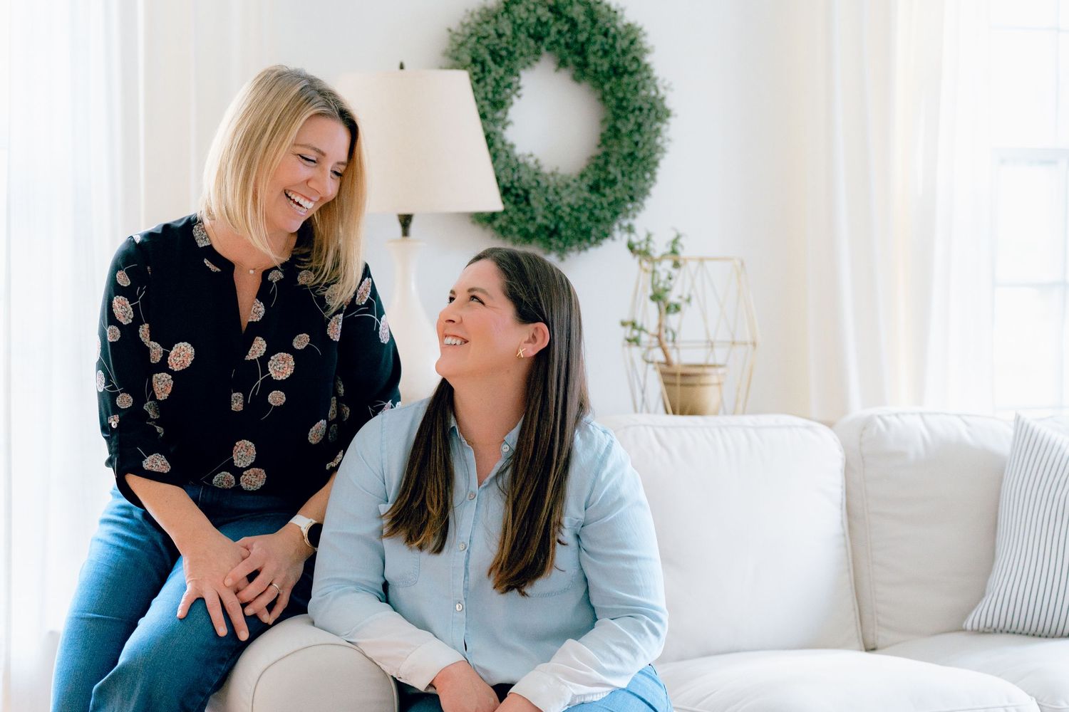 Two sisters share a joyful moment laughing together on a white couch for this brand session in Hudson, Ohio.
