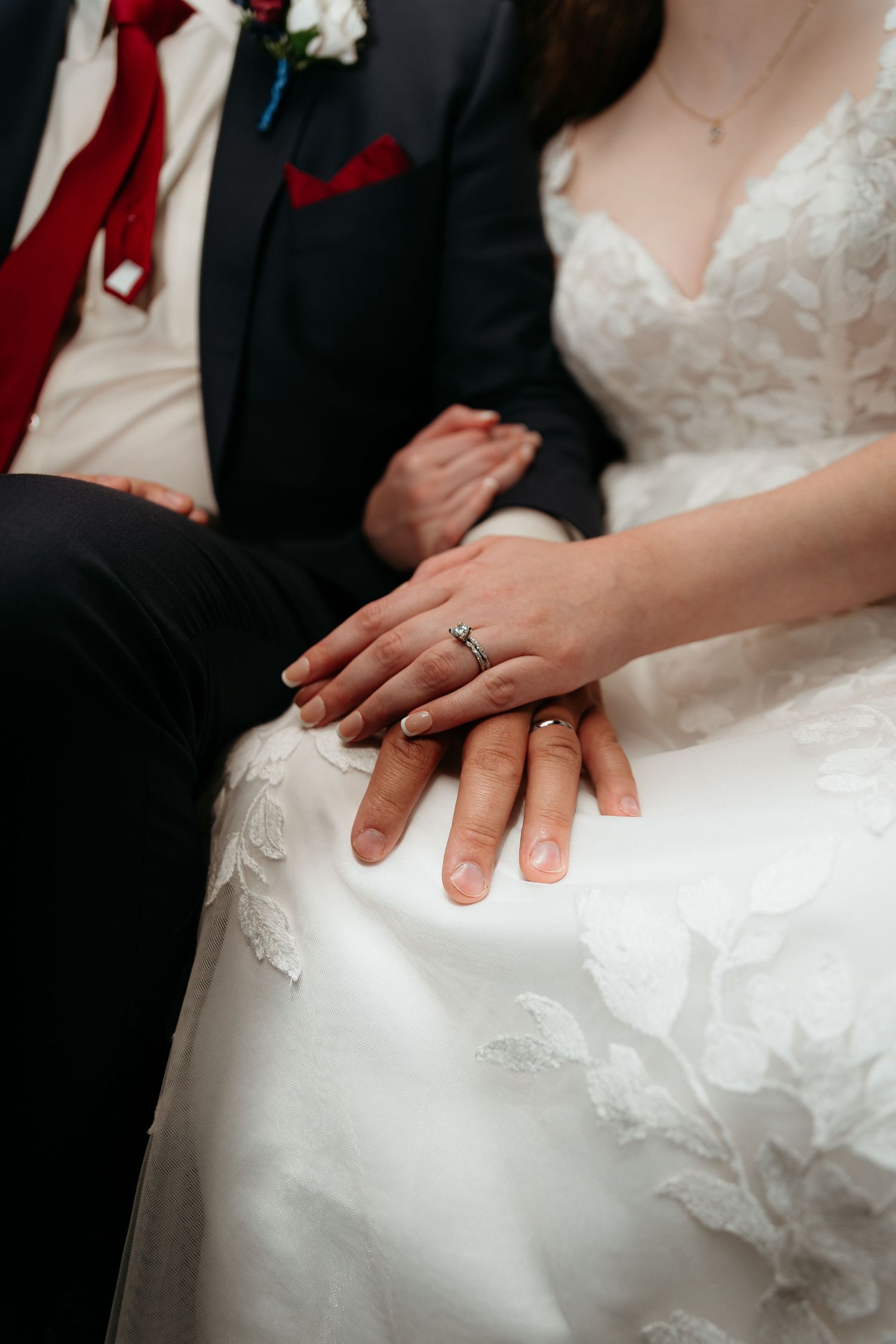 Close-up of newlywed couple's hands with engagement ring resting on white wedding dress.