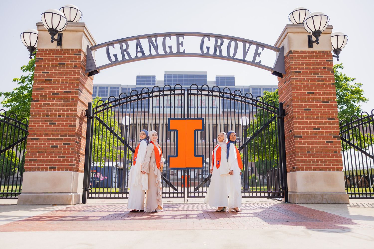 Group of UIUC graduation girls posing together in front of the Grange Grove gate and Memorial Stadium