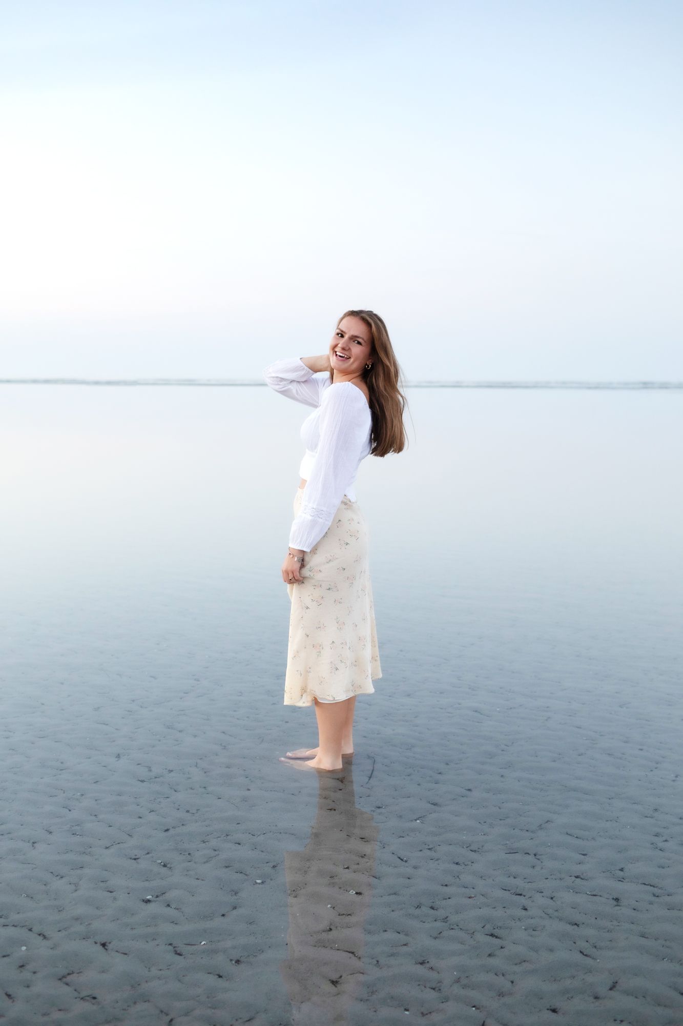 Senior girl wears white blouse and yellow floral midi dress at sunset at Wingaersheek Beach in North Shore Gloucester for senior portraits.
