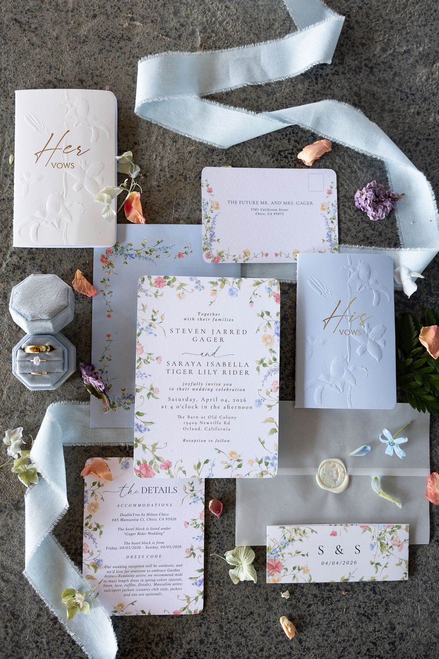 Elegant wedding invitation suite with floral watercolor designs, silk ribbon, and calligraphy details on gray background.