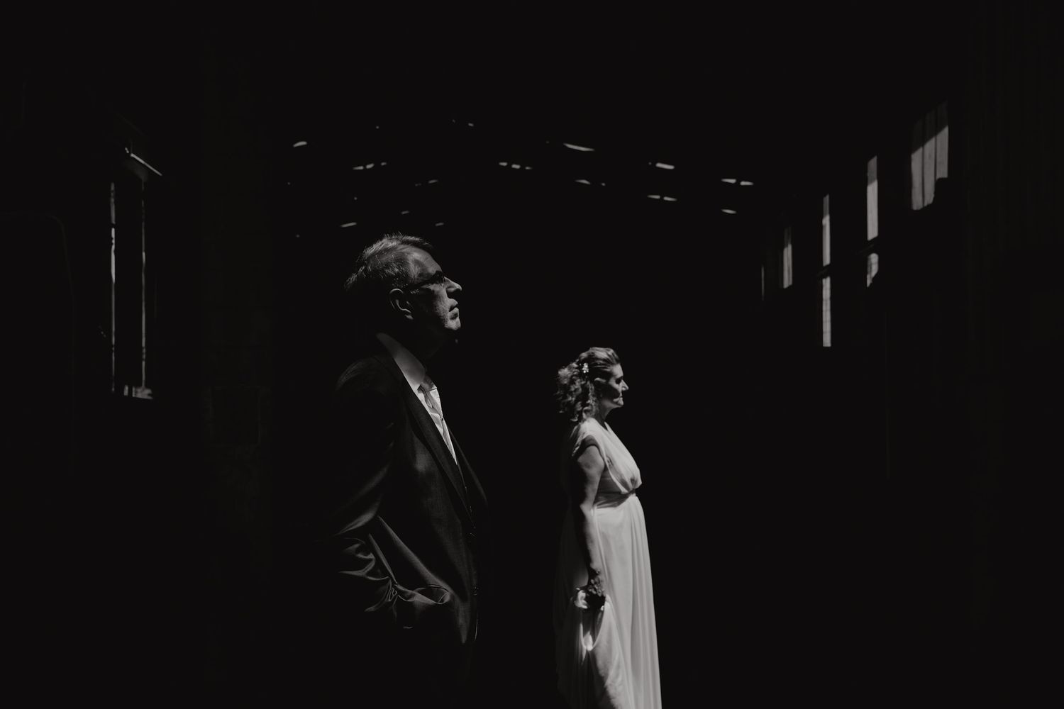 Arty and dramatic wedding photo of bride and groom standing side by side in silhouette with moody lighting and high contrast – creative.
