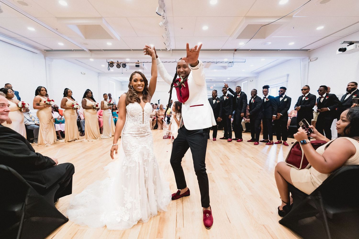 A couple celebrates joyfully during their wedding reception on a polished wooden dance floor surrounded by guests.