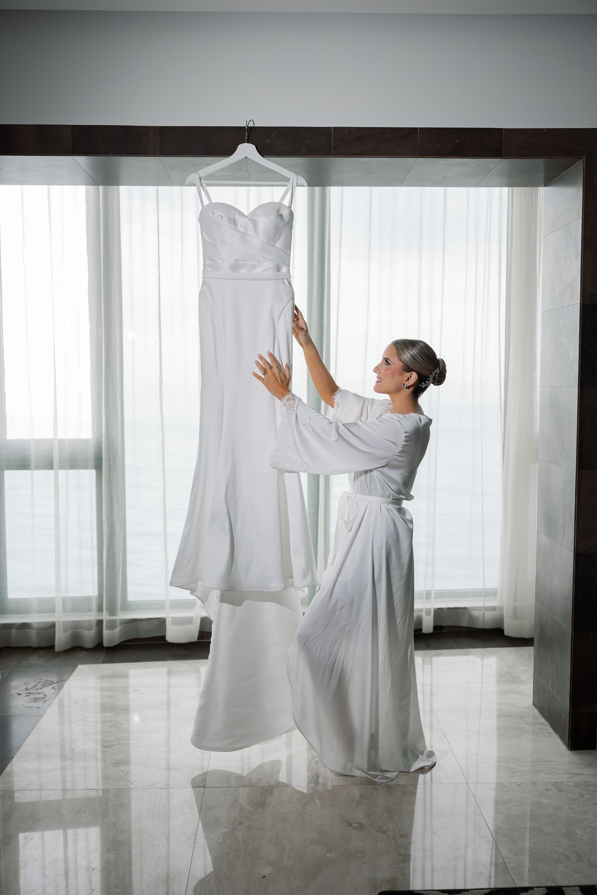 A woman in a white wedding dress holds up her dress while standing in a room.