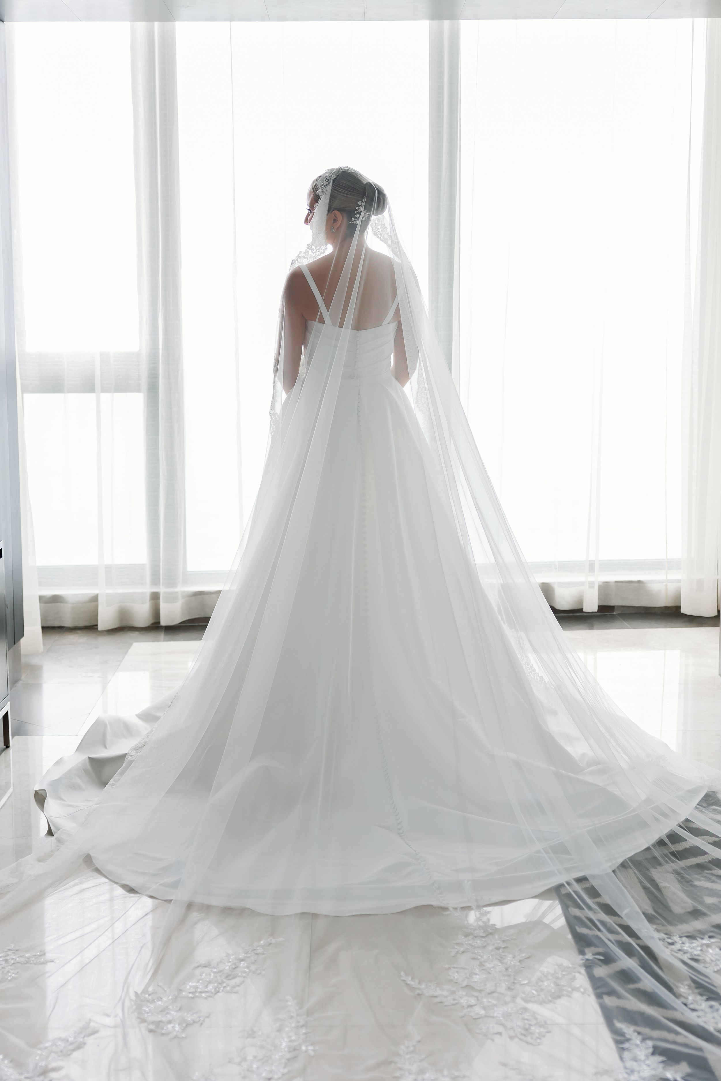 A woman in a white wedding dress stands in a room, facing away from the camera.