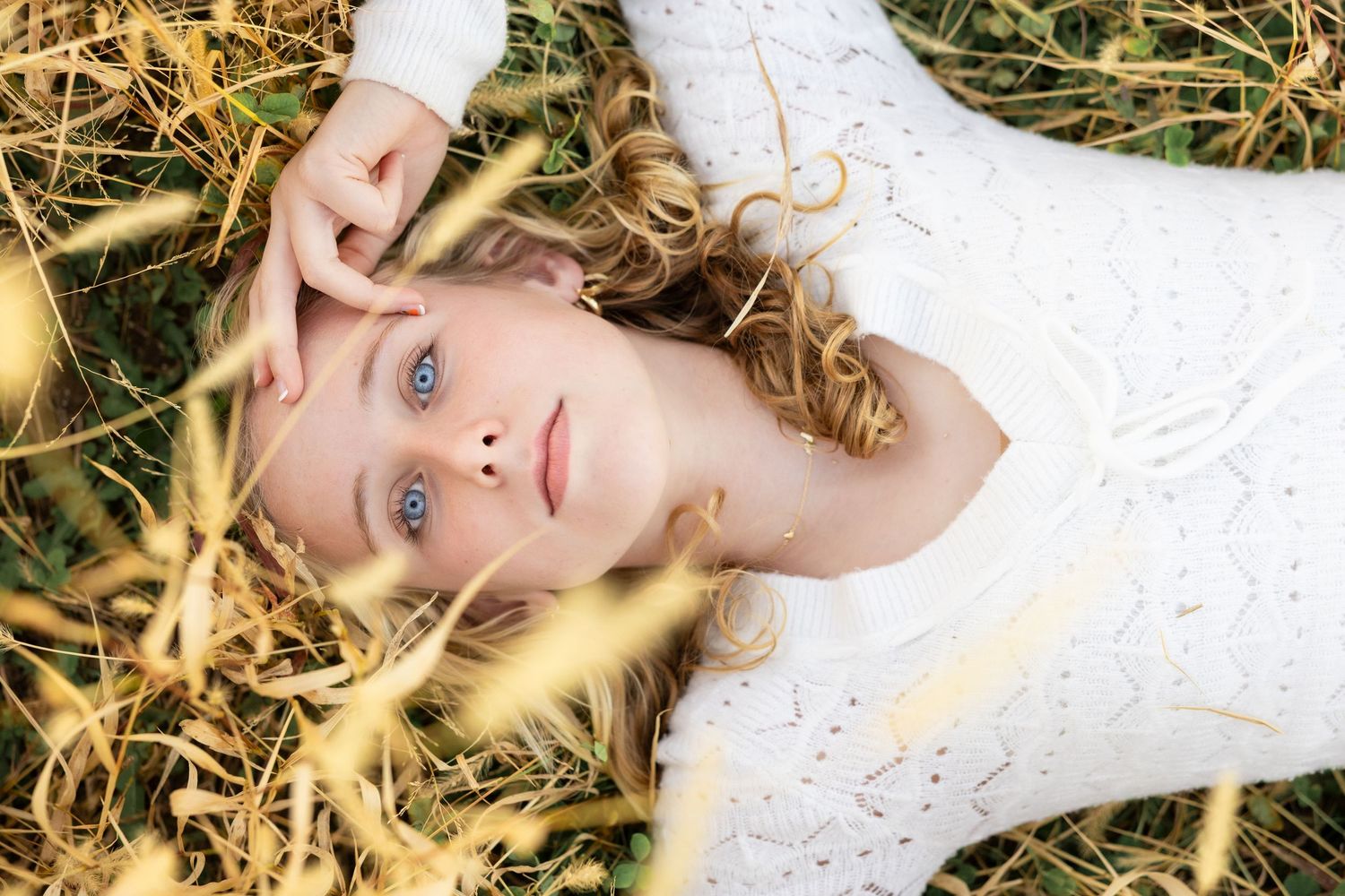 Person in white lace dress lying in golden autumn grass with dreamy expression.