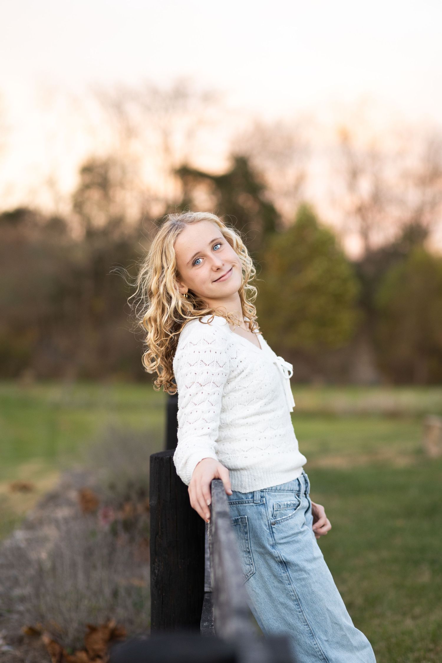A child in a white sweater and jeans dances joyfully in a grassy field at sunset.