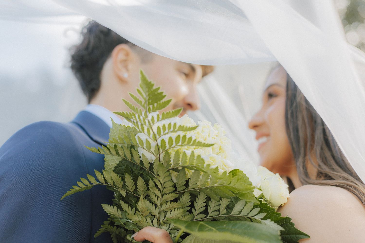 Close-up shot of a couple embracing with green ferns in the foreground creating a romantic atmosphere.